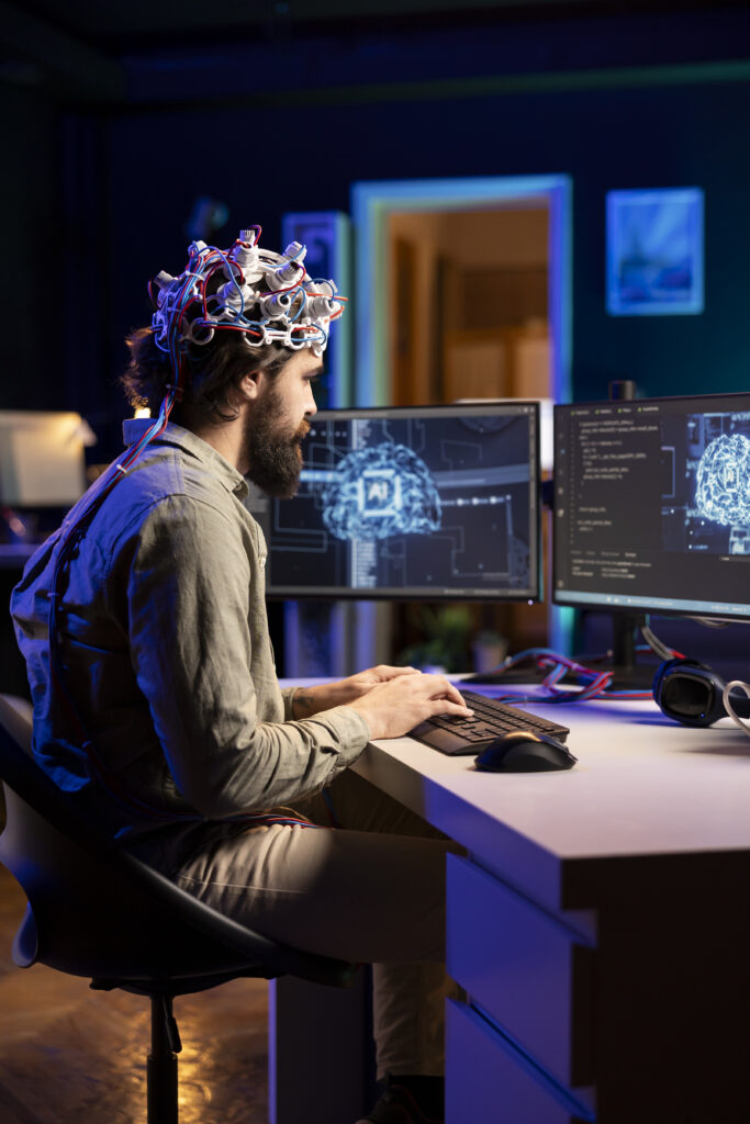 Software developer with EEG headset on writing code allowing him to transfer mind into computer virtual world, becoming one with AI. Transhumanist using neuroscientific tech to gain superintelligence